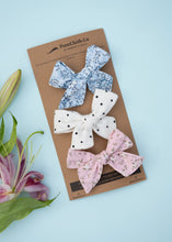 Load image into Gallery viewer, An image of three elegant knot combo hairclips for girls, one in white colour with small black dots, the other in a pinkish flowery print, and a third with light blue floral print, on a light blue background.