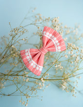 Load image into Gallery viewer, An image of a pink lace bow hair accessory, with pretty white print throughout, on a serene light blue background.