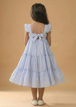 Load image into Gallery viewer, Child wearing a blue and white striped dress with a ruffled back on a beige background