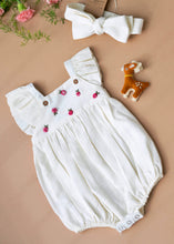 Load image into Gallery viewer, A white baby girl dress with head band and a cute little deer-friend is kept on a light peach background with some flowers aside.