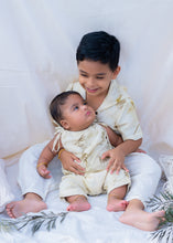 Load image into Gallery viewer, A boy holding small kid A kid wearing a cotton jumpsuit eco-printed with silver oak leaves on it sitting on a bed.