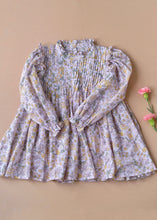 Load image into Gallery viewer, A beautiful lavender fairy floral baby girl dress with frills at the neck kept upon a peach background with some flowers aside