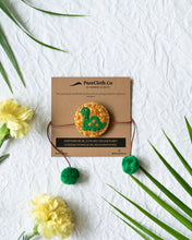 Load image into Gallery viewer, Handmade Dinosaur Rakhi wrapped around brown card with flower and leaf aside.