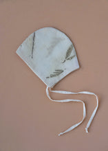 Load image into Gallery viewer, A kidswear bonnet with a silver oak leaves on it kept upon a pink background.
