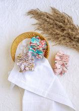 Load image into Gallery viewer, hair accessories of three Floral Scrunchies placed in a wooden basket with a white cloth beneath, placed on a white background with some leaves for decoration