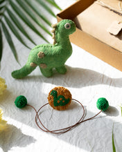 Load image into Gallery viewer, Handmade Dinosaur Rakhi wrapped around brown card with a brown gift box, cute green dinosaur, flower and leaf aside.