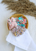 Load image into Gallery viewer, hair accessories of three Floral Scrunchies placed in a wooden basket with a white cloth beneath, placed on a white background with some leaves for decoration