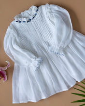Load image into Gallery viewer, The pintuck detailing across the bust and ruffles running across the neckline in classic white palette kept upon a peach background with some leaf and flower aside.