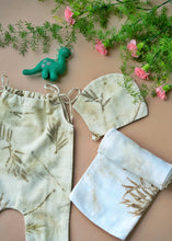 Load image into Gallery viewer, A beautiful unisex newborn gift hamper with swaddle made of wild silver oak with a toy kept upon a peach background with some flowers and leaves kept aside.