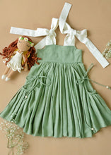 Load image into Gallery viewer, An elegant and beautiful secret fairy pocket dress for baby girl dresses kept on a peach background with some flowers and toy aside.