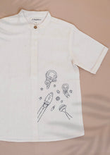 Load image into Gallery viewer, A white coloured Organic Cotton Doodle Shirt kidswear with space theme design kept on a biege coloured background