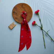 Load image into Gallery viewer, A beautiful red silk hair scrunchie kept upon a round wooden log with some flowers and brown card aside.