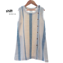 Load image into Gallery viewer, A beautiful white A-line shift dress with flattering vertical blue stripes and laced hemline is hanged using hanger.