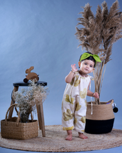 Load image into Gallery viewer, A baby girl wearing a jumpsuit with matching hair accessories with some artificial plants and wooden pots and with some rabbit toys and a flower basket aside.