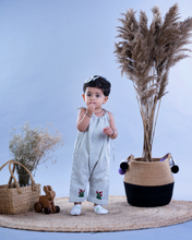 Load image into Gallery viewer, A baby girl wearing cute jumpsuit with matching hair accessories with some artificial plants and wooden pots and with some rabbit toys and a flower basket aside.
