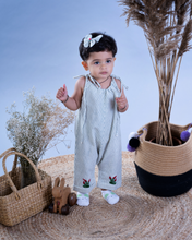 Load image into Gallery viewer, A baby girl wearing cute jumpsuit with matching hair accessories with some artificial plants and wooden pots and with some rabbit toys and a flower basket aside.