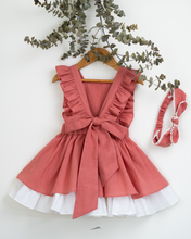 Load image into Gallery viewer, A back view of a beautiful dress with a criss-cross back hung on a hanger with a matching hair accessory beside it with a stem of leaves upon it.