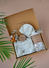 Load image into Gallery viewer, A beautiful gift box filled with unisex newborn gift hamper with swaddle made of wild silver oak with a toy and some flowers inside the box which is kept upon a pink background with some leaves aside.
