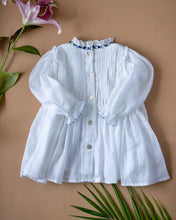 Load image into Gallery viewer, The pintuck detailing across the bust and ruffles running across the neckline in classic white palette kept upon a peach background with some leaf and flower aside.
