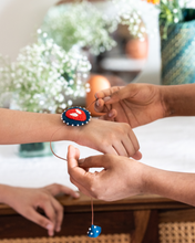 Load image into Gallery viewer, A man tying a handmade spiderman rakhi to child with some furniture in the background. 
