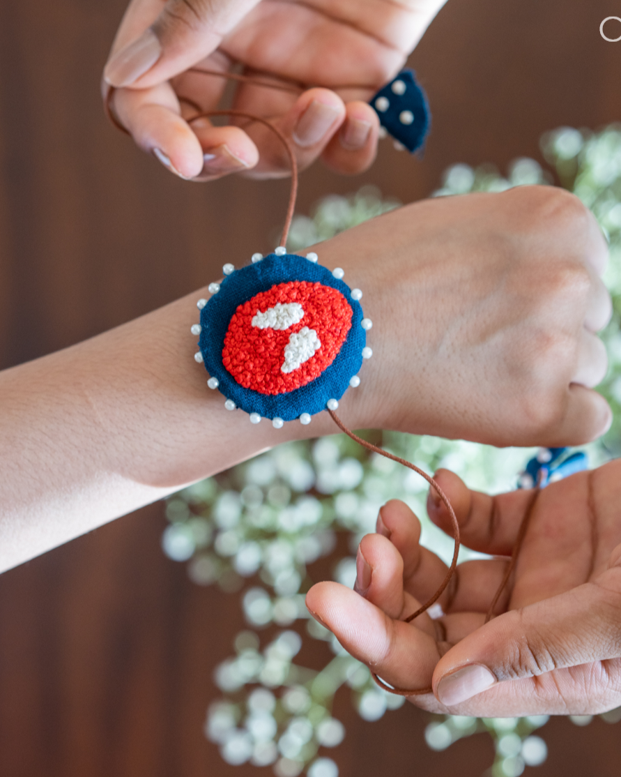 A man tying a handmade spiderman rakhi to child with some flower in the background.