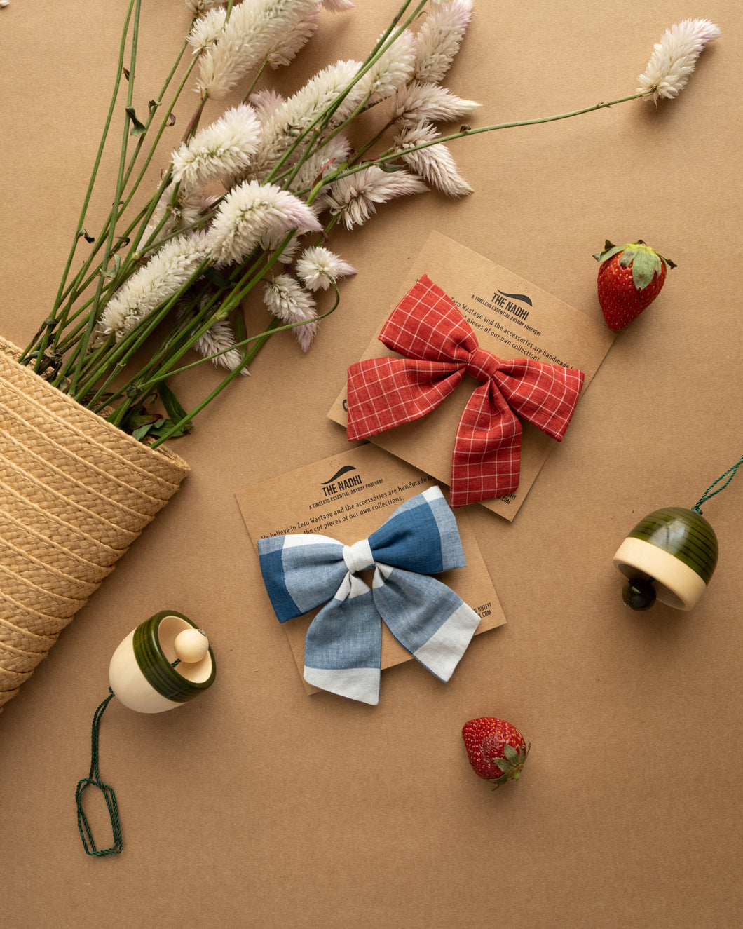 Two different bow type hair accessories placed on a brown background with a cute small flowers and strawberry aside.