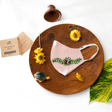 Load image into Gallery viewer, A beautiful organic embroidery face mask kept on a wooden plate with tortoise, flowers, cards and leaf aside.
