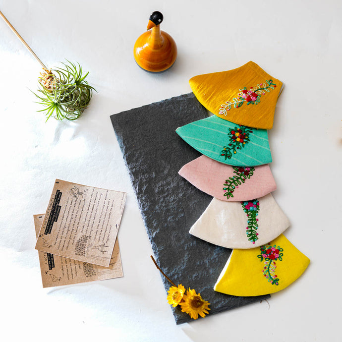 A beautiful colouful organic embroidery face masks kept on a grey sheet with some cards, flower and toy aside.