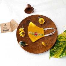 Load image into Gallery viewer, A beautiful organic embroidery face mask kept on a wooden plate with tortoise, flowers, cards and leaf aside.
