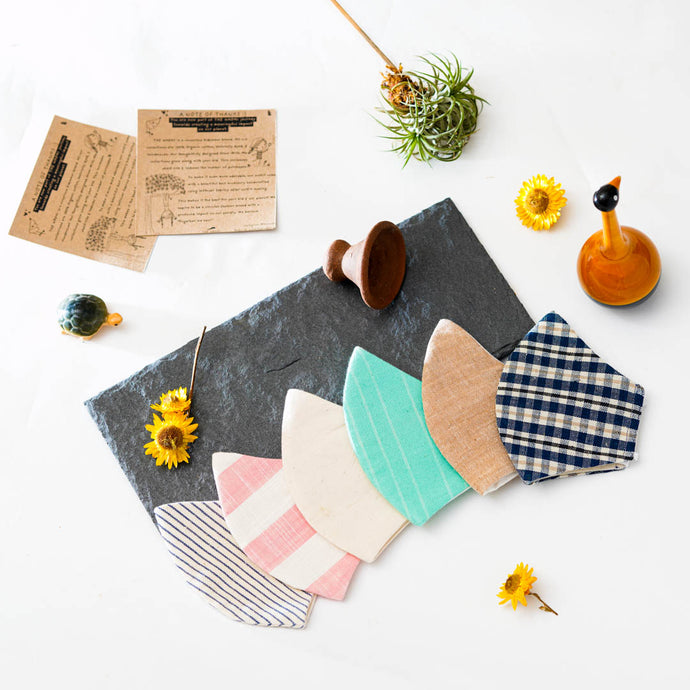 A different color and multi-patterned face masks kept upon a grey sheet with some flower, toys and cards aside.