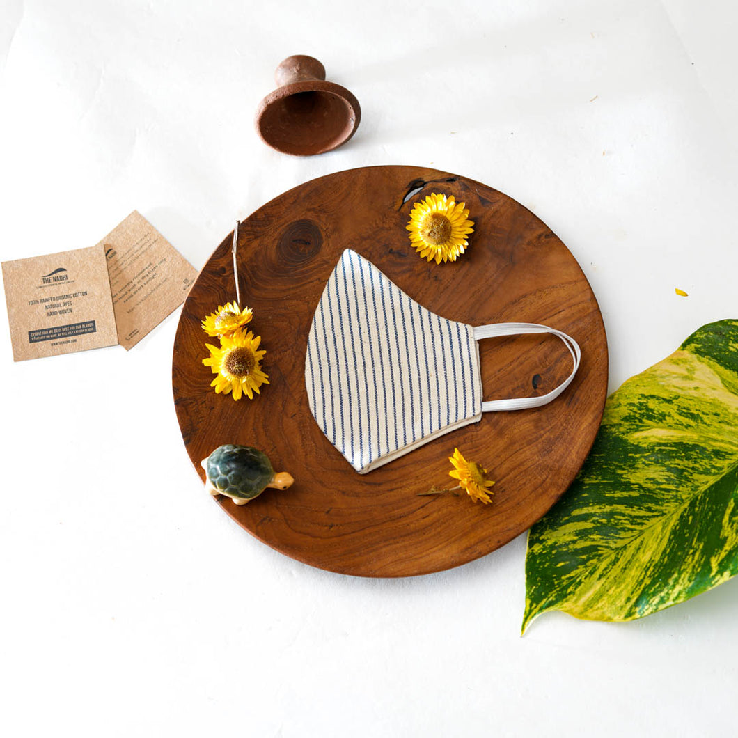 A beautiful, patterned face mask kept upon a round wooden log with some flower, leaf, toys and cards aside.